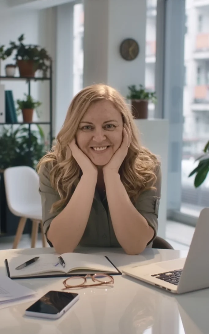 Leader cradling her face, smiling beside a journal and laptop — aligning her internal narrative with her external systems