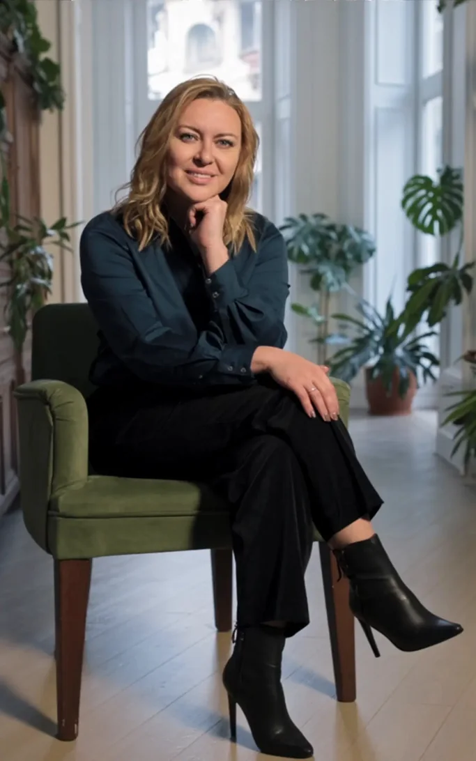 Andrea Florescu seated in a green velvet chair, hand on chin, confident and grounded — a strategist at ease with her decisions